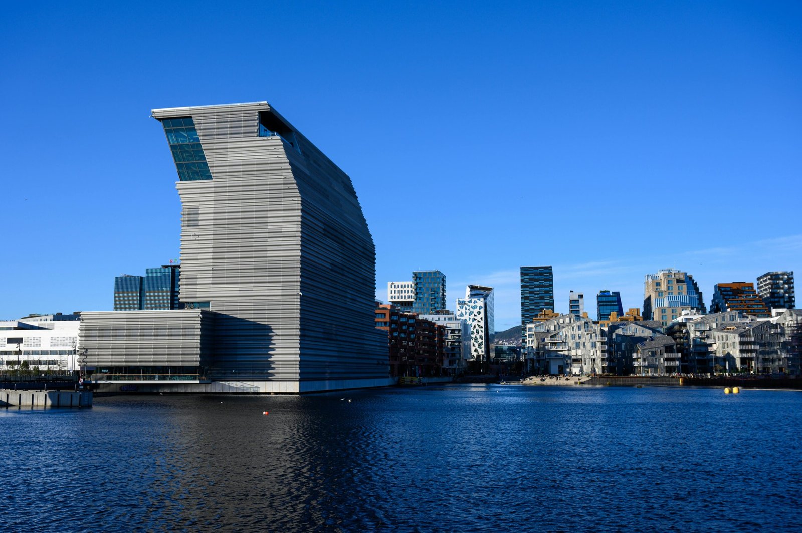 Stunning view of the contemporary Munch Museum and Oslo skyline reflected on the waterfront under a clear blue sky.